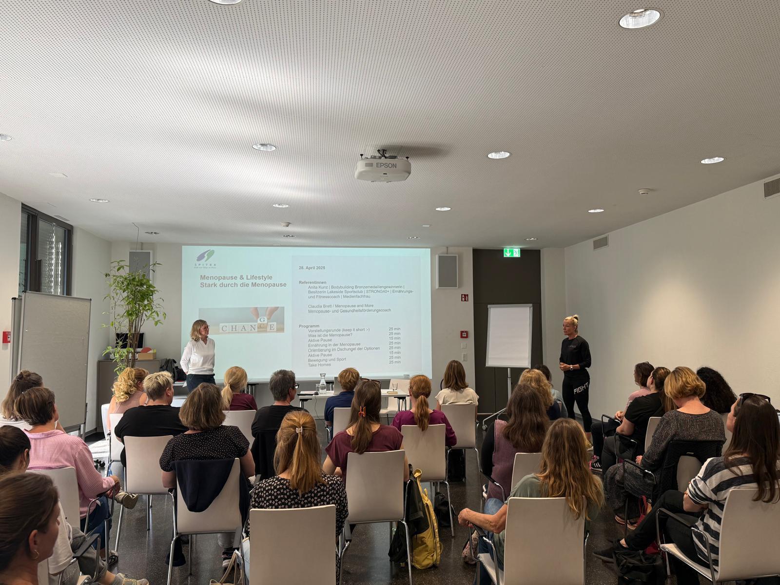Claudia presenting a menopause awareness talk to a seated audience.